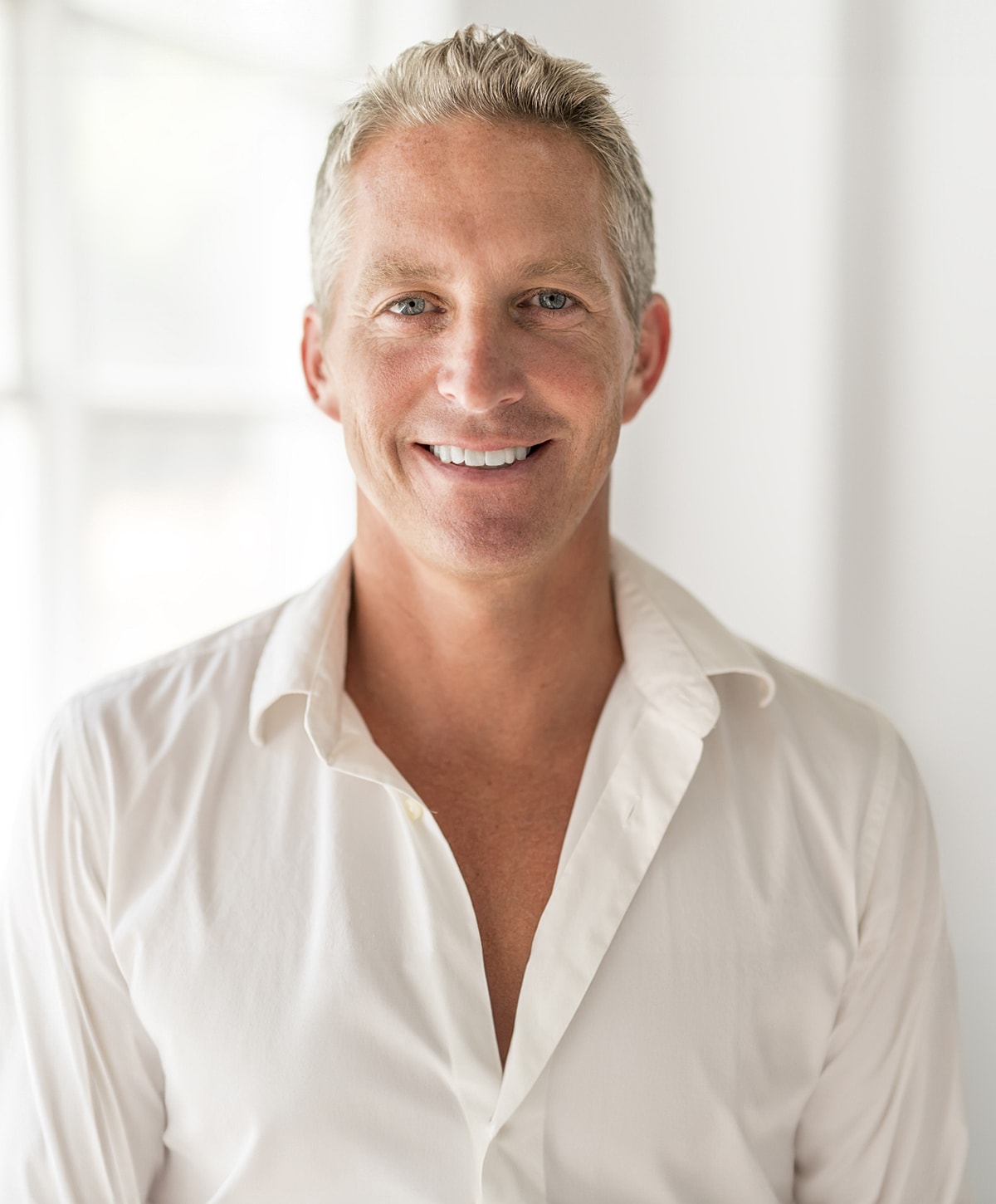 Smiling man in white shirt, bright background.