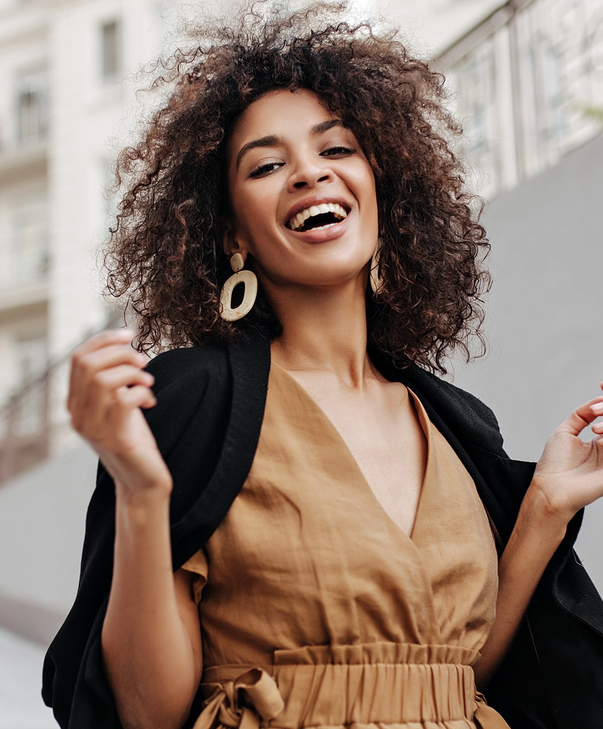 Smiling woman with curly hair in stylish outfit.